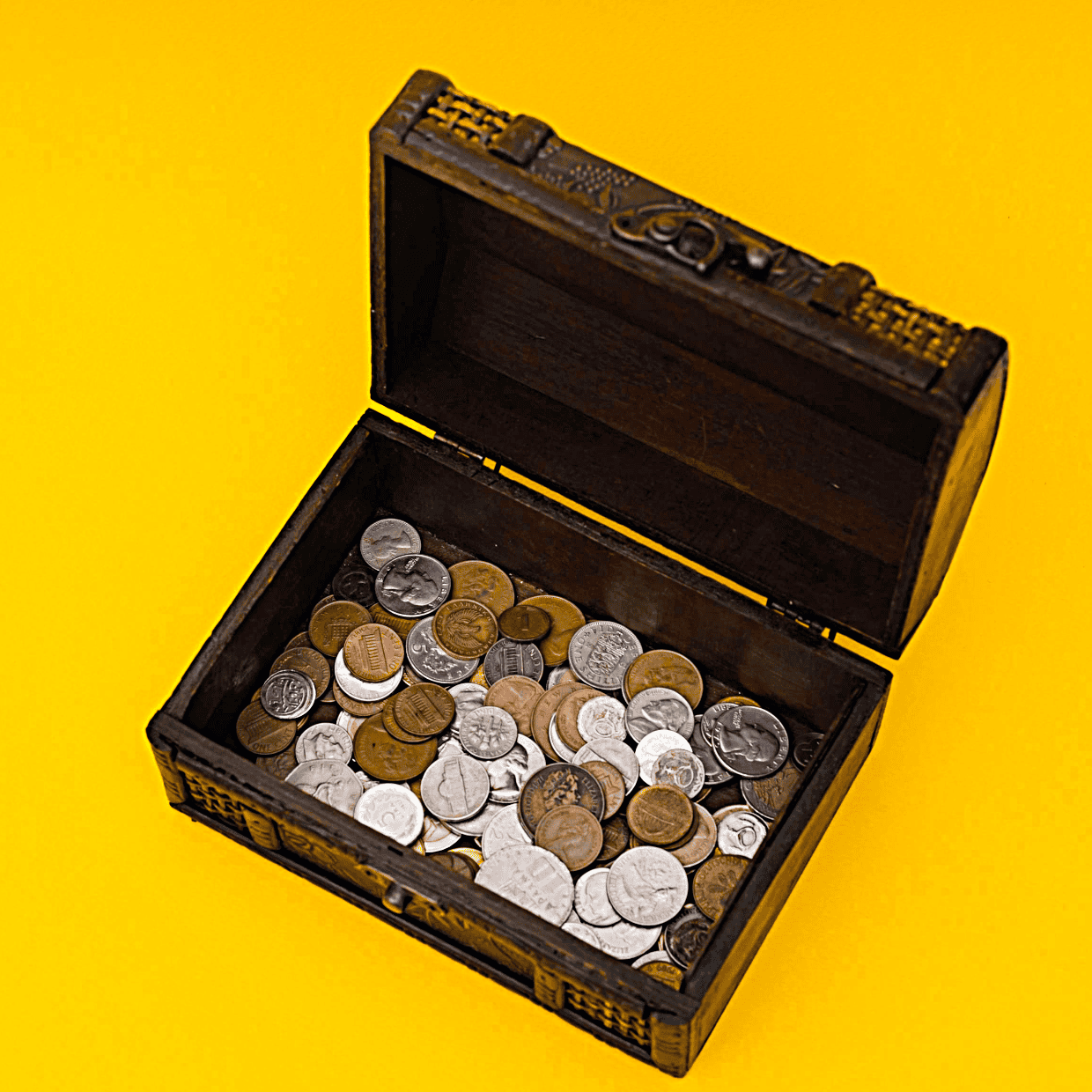 Open wooden chest filled with assorted coins on a bright yellow background.