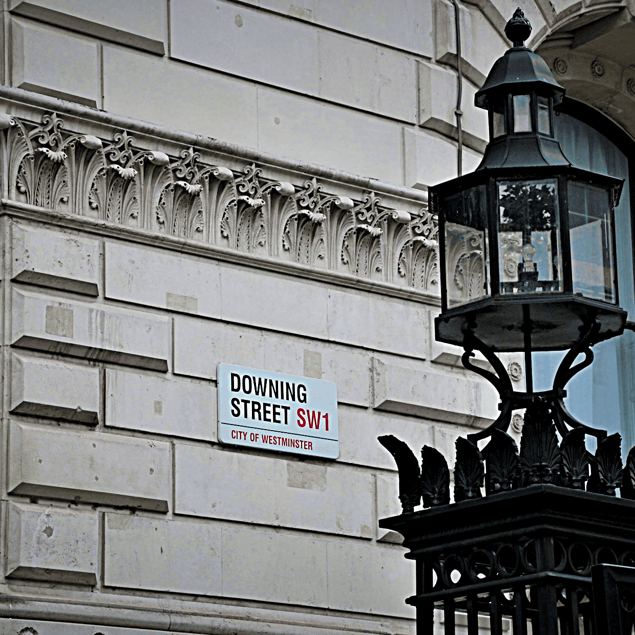 Street sign reading “Downing Street SW1” on a stone building in Westminster, with a traditional black lantern in the foreground.