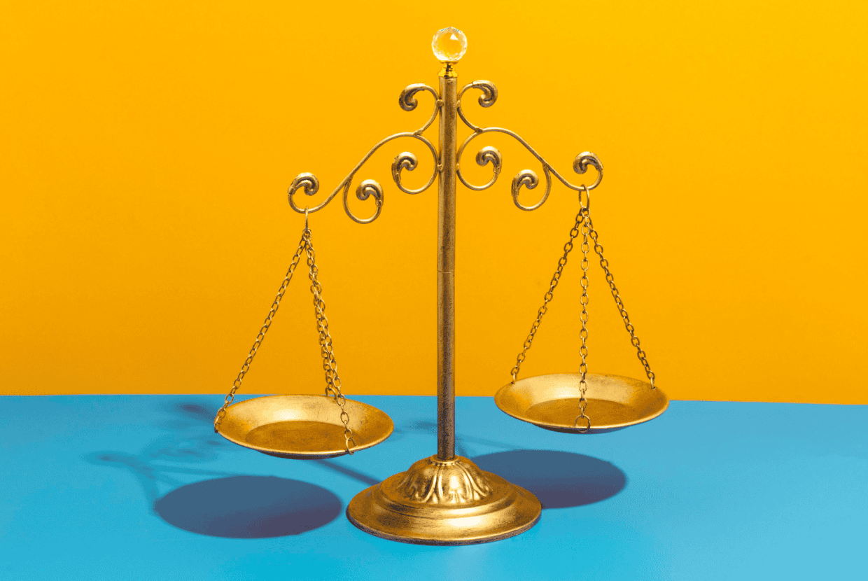 Decorative golden balance scales standing on a blue surface against a bright yellow background.