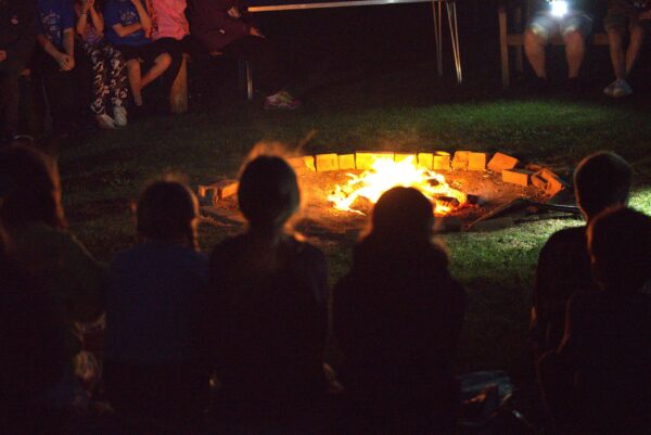 Photo of people sitting around a campfire at night, representing fellowship, community, and shared activities within a church or group.
