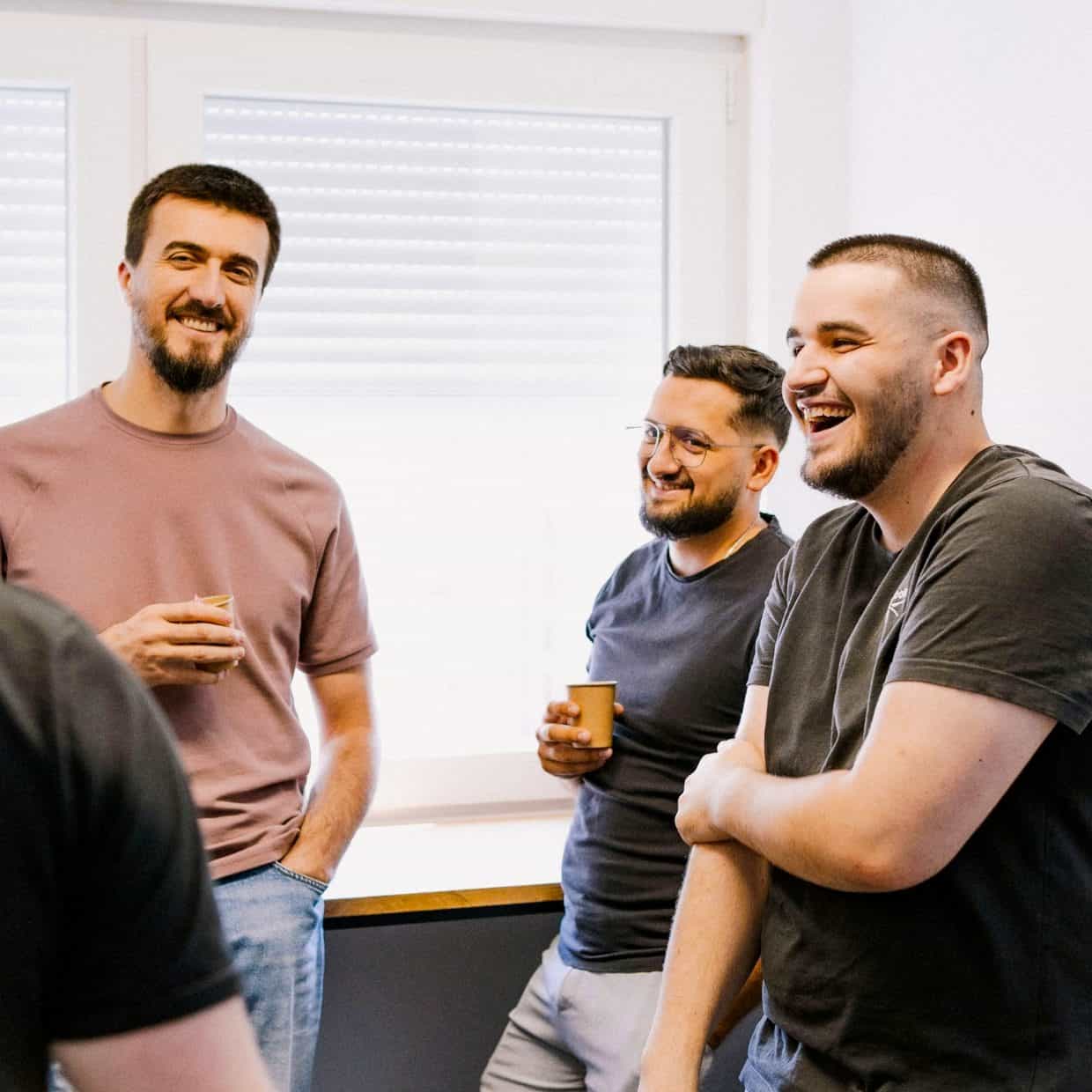 Group of men laughing and chatting together while holding coffee cups in church office.