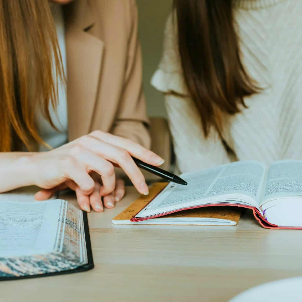 Two people studying together at a table, with one pointing at a passage in an open Bible.