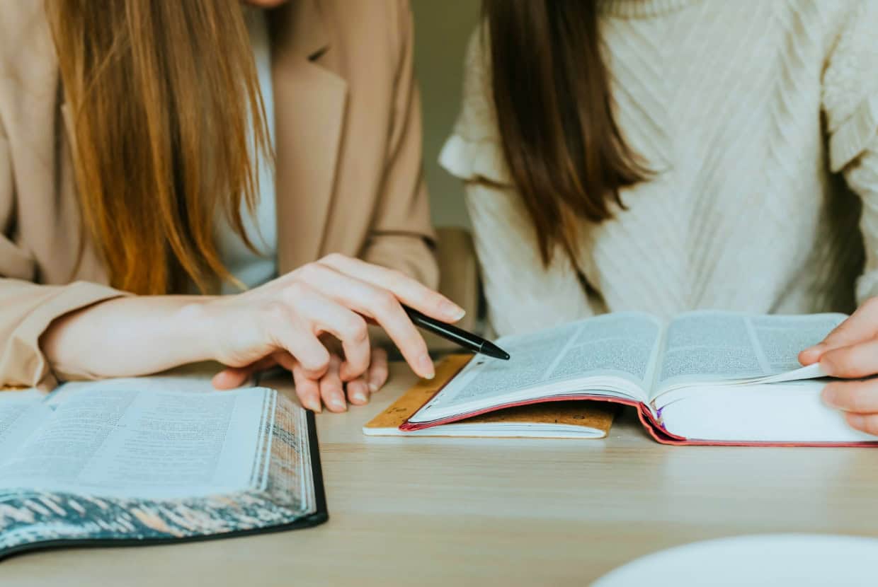 Two people studying together at a table, with one pointing at a passage in an open Bible.