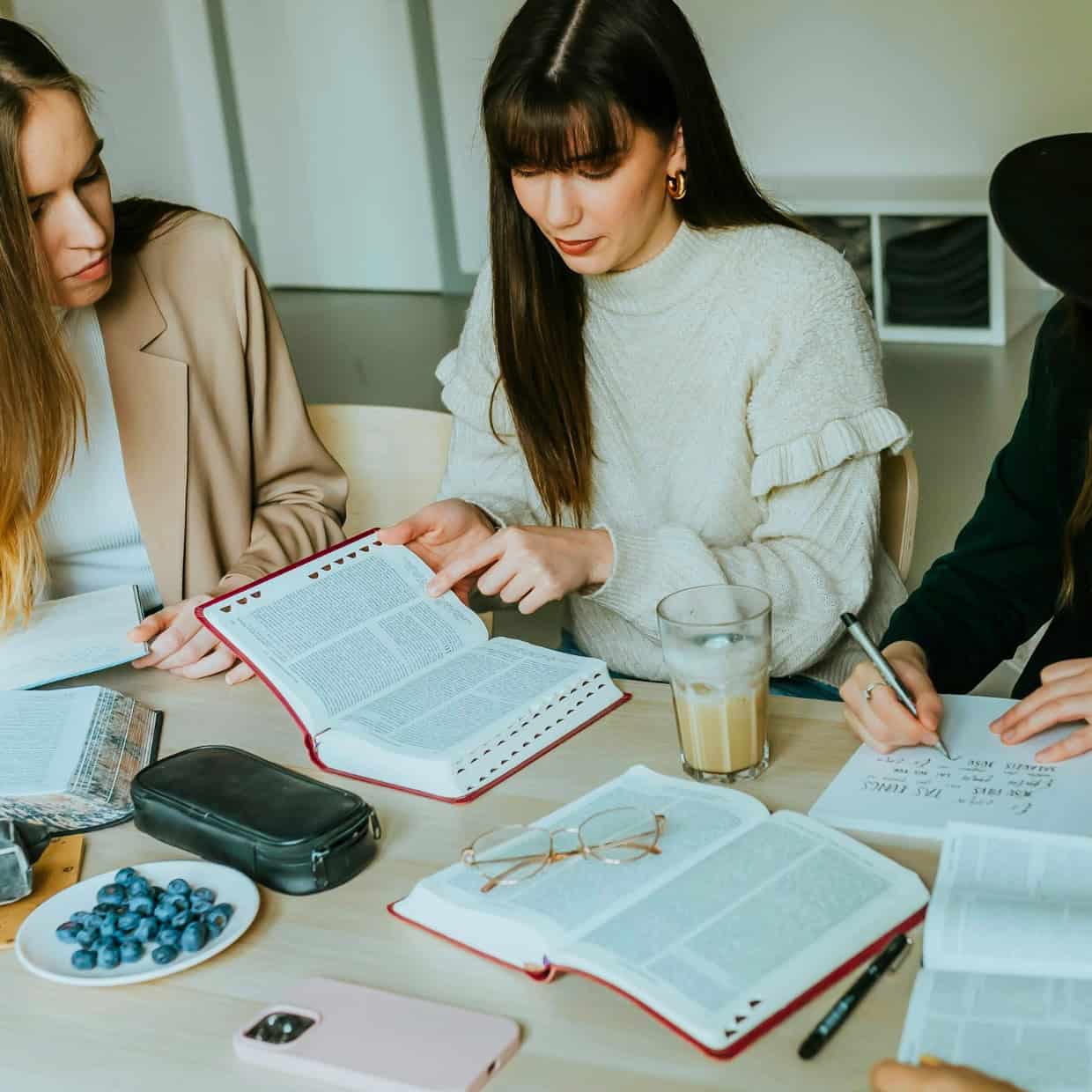 Group of young women sitting around a table studying together with open Bibles and notebooks.