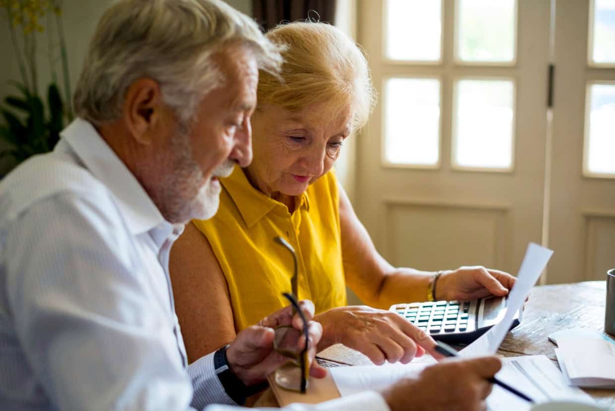 Couple sitting at a table reviewing financial documents together, with a calculator and papers spread out in front of them.