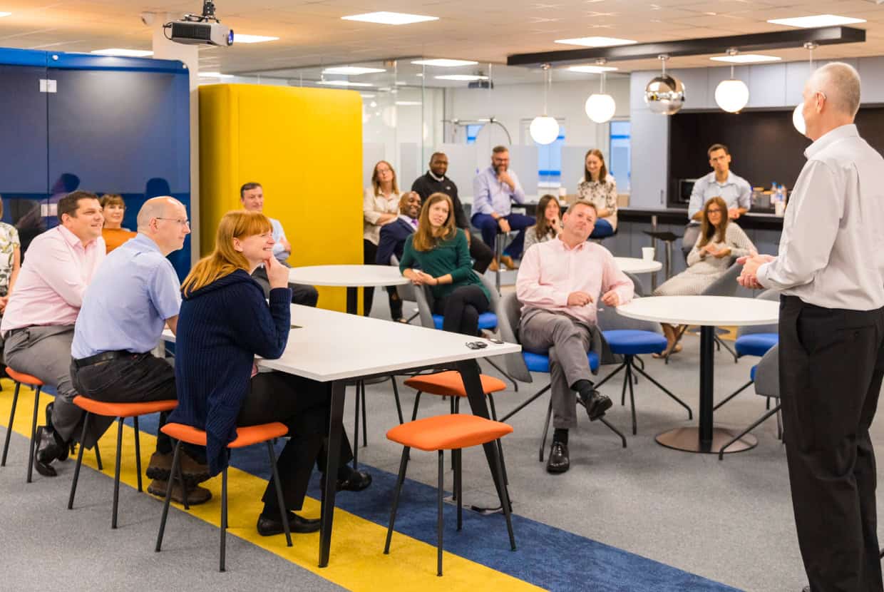 A group of professionals listening to a speaker during an office meeting or presentation.