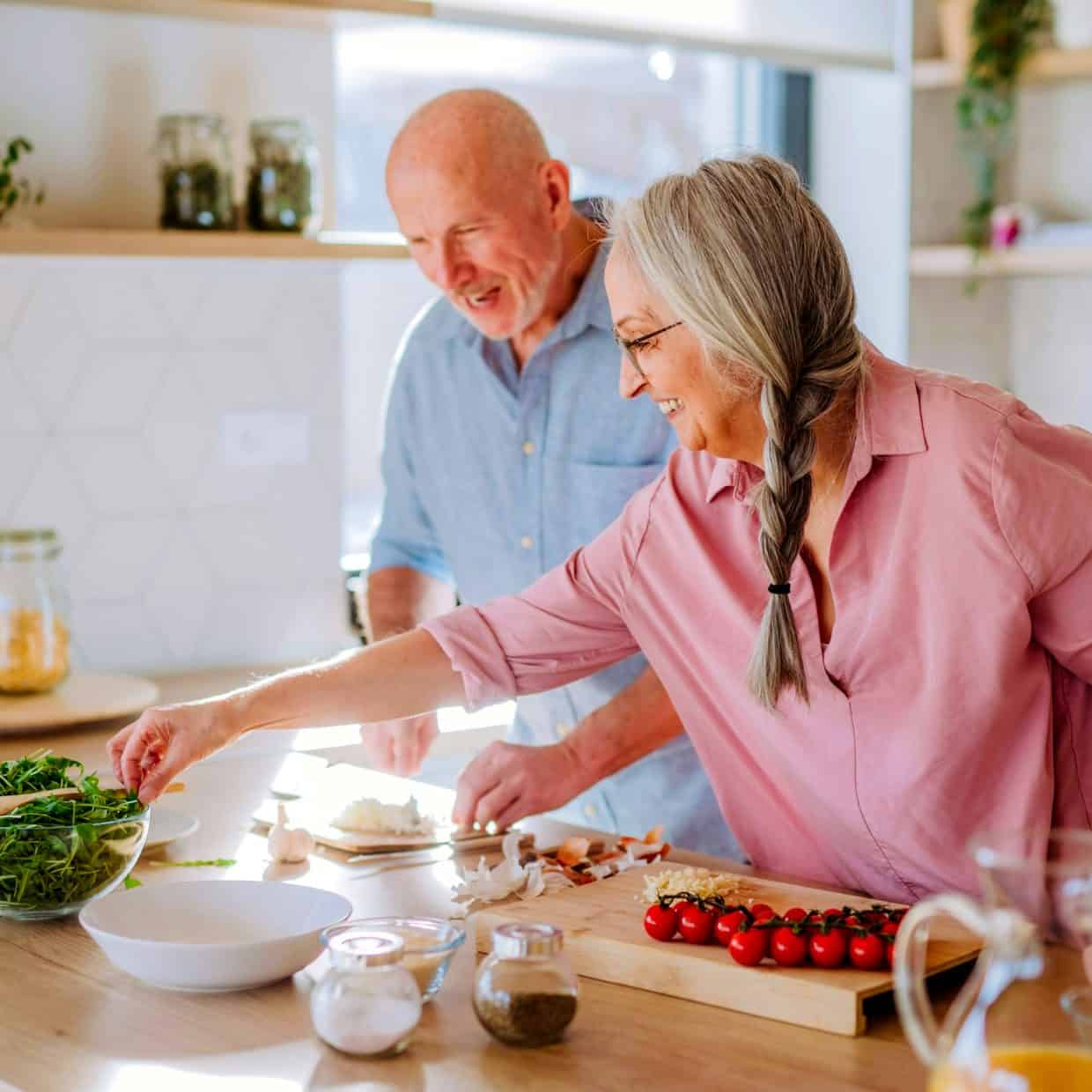 Smiling older couple preparing a meal together in a bright, modern kitchen.
